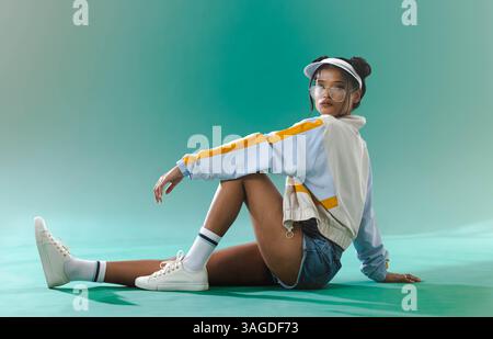 Fashionable woman in sporty outfit sitting confidently on studio floor. activewear, confidence, sportswear, model, trendy, athletic Stock Photo