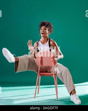 Joyful woman laughing while sitting playfully on chair in stylish studio. Female, happiness, fashion, lifestyle, cheerful Stock Photo