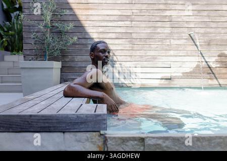 Relaxing in pool, African American African American man enjoying morning swim, feeling refreshed. Swimming, relaxation, leisure, poolside, wellness, v Stock Photo