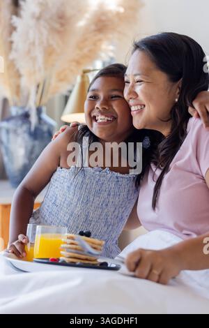 Mother and daughter enjoying breakfast together, smiling and embracing at home. Family, bonding, relationship, kitchen, morning, happiness Stock Photo