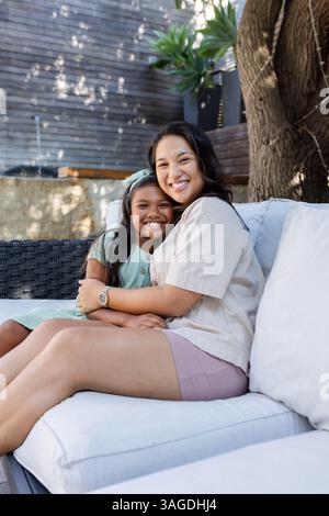 Smiling mother and daughter sitting on outdoor sofa, enjoying sunny day together. Family, bonding, happiness, relaxation, leisure, outdoors Stock Photo