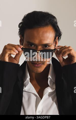 Confident man adjusting sunglasses, wearing stylish black jacket and white shirt. Fashion, style, confidence, menswear, eyewear, trendy Stock Photo
