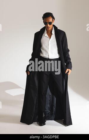 Confident man in stylish black coat and sunglasses posing in studio. Fashion, style, confidence, elegance, urban, modern Stock Photo