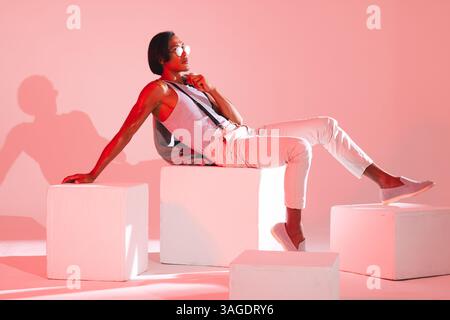 Stylish man in glasses posing confidently on white cubes in modern studio. Fashion, confidence, eyewear, portrait, trendy, male Stock Photo