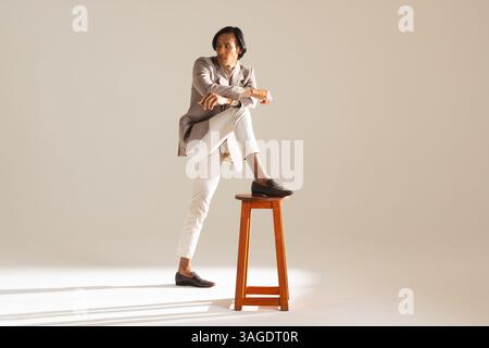 Confident man in stylish outfit posing with one leg on wooden stool. Fashion, style, confidence, menswear, trendy, standing Stock Photo