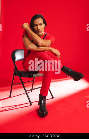 Confident man in red outfit sitting on chair in fashion studio. style, menswear, trend, attire Stock Photo