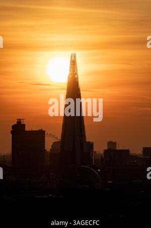 The Shard skyscraper silhouetted against a vivid orange sunset in London, United Kingdom, with the sun setting behind the building and the London Eye Stock Photo