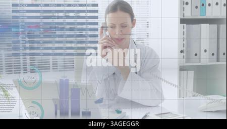 Financial data processing against female caucasian doctor taking notes while talking on phone Stock Photo
