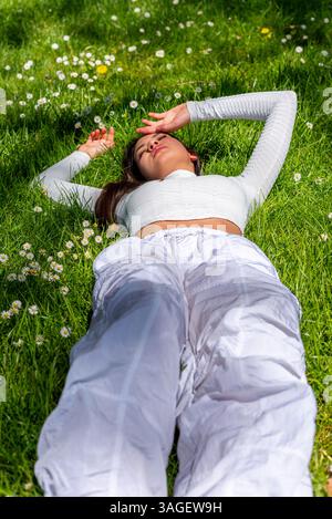 Young woman lying down and relaxing on the grass between many beautiful daisies Stock Photo