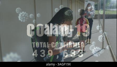 Covid-19 text with increasing cases against school boy wearing face mask using smartphone Stock Photo