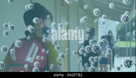 Multiple covid 19 cells floating against school boy wearing face mask standing in a queue at school Stock Photo