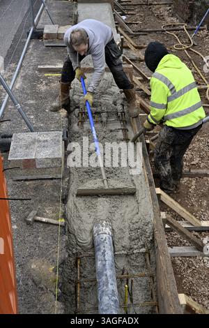 Builders levelling pumped concrete going into timber shuttered steel reinforced beam and compacting with vibrating machine on building site Stock Photo