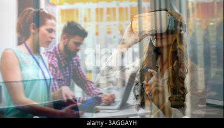 Using virtual reality headset, woman interacting with digital interface over office workers Stock Photo