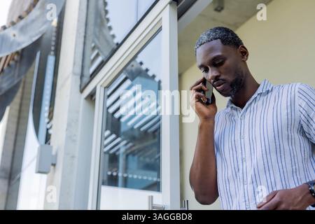 African American African American man talking on smartphone outside modern building, looking focused. Business, communication, technology, urban, corp Stock Photo