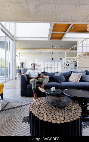Relaxing at home, man sitting on sofa enjoying coffee in modern living room. Relaxation, leisure, comfort, lifestyle, interior, casual Stock Photo