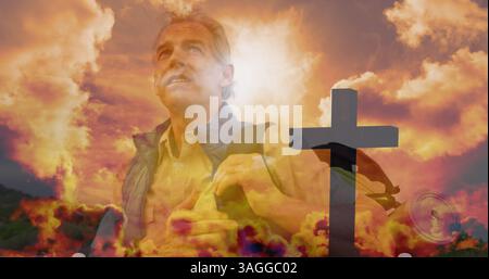 Senior caucasian man hiking over fast moving clouds and cross during sunset Stock Photo