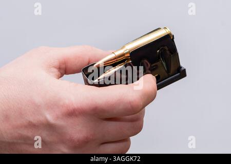 A male hunter loads cartridges for a rifle magazine on a light background, equip a combat weapon Stock Photo
