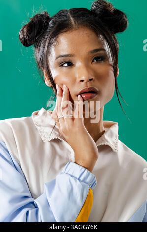 Thoughtful young woman with stylish hair touching face in grunge studio. Contemplation, hairstyle, fashion, portrait, alternative, edgy Stock Photo