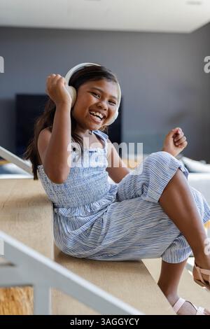 Smiling girl enjoying music with headphones, sitting on staircase at home. Listening, relaxation, lifestyle, casual, leisure, happiness Stock Photo