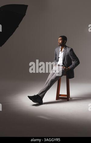 Confident man in stylish suit sitting on stool in professional studio. Portrait, fashion, confidence, formal, elegance, attire Stock Photo