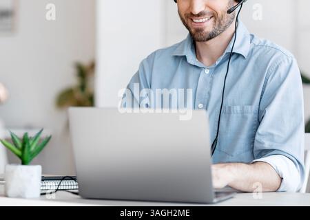 Call center operator at work. Male manager wearing headset and using laptop Stock Photo