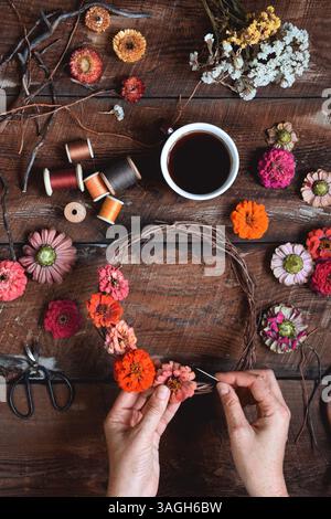 Overhead shot of female hands making a flower wreath on a rustic wooden table Stock Photo