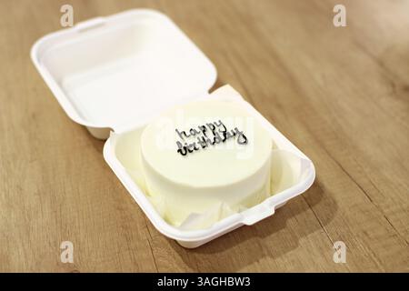A white cake with black frosting and the text Happy Birthday written on it. Wooden background Stock Photo