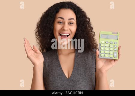 Young African-American woman with calculator on beige background Stock Photo