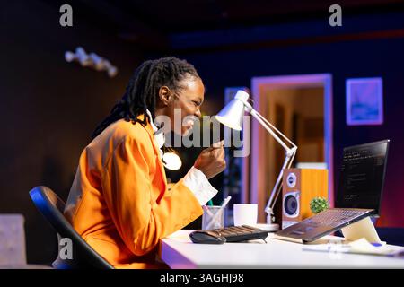 Joyous programmer at desk typing code on laptop, delighted after successfully developing software program. Thrilled african american woman at home excited after implementing new features Stock Photo