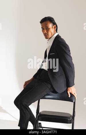 Confident man in black suit sitting on chair, looking at camera. Fashion, portrait, confidence, elegant, formal, businessman Stock Photo