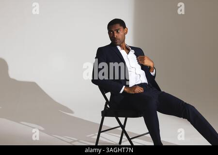 Confident man in stylish suit sitting on chair, looking away thoughtfully. Business, fashion, leadership, elegance, contemplation, thinking Stock Photo