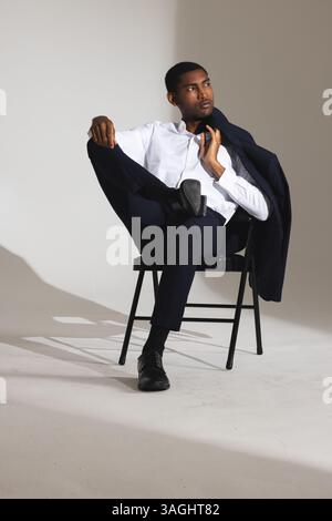Confident man in stylish suit sitting on chair, looking thoughtfully aside. Business, professional, confidence, fashion, executive, corporate Stock Photo