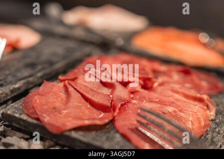 Close Up of Sliced Cured Meat on Dark Stone Platter with Fork Stock Photo