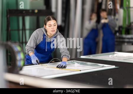 Young woman measuring sheet of glass in factory Stock Photo