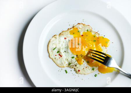 A single fried egg with broken yolk in a white plate isolated on a white background. Healthy food concept. Directly above. Stock Photo