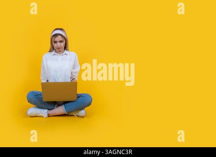 Unhappy caucasian woman sit floor hold use laptop looking camera angrily. Yellow background, copy space. Having problems, reading negative news. Stock Photo