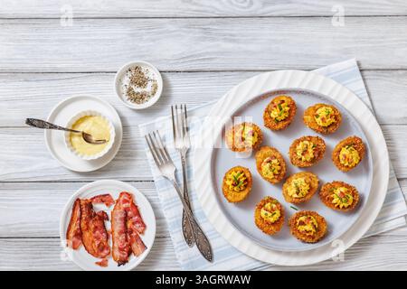 Deep fried deviled eggs with crispy coating of panko and parmesan, sprinkled with fresh chives and crumbled bacon on white plate on wooden table with Stock Photo
