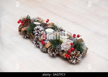Decorative holiday centerpiece featuring pinecones, red berries, evergreen sprigs, and tealight candles arranged for festive table decor. Stock Photo