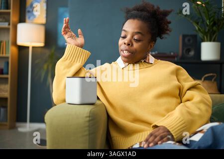 African American Woman Interacting with Smart Speaker Stock Photo