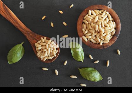Pine nuts overhead shot with a close up top view of many shelled pine nuts in a wooden spoon and in a bowl on a dark grey background. Stock Photo