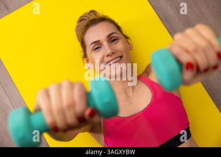 dumbbell exercises. woman is laying down on fitness mat and doing workout at home. top view Stock Photo