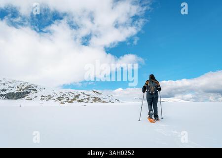 Rear view of a woman snowshoeing across a snow-covered expanse in Sierra de Gredos, Spain. Wearing a backpack and using trekking poles Stock Photo