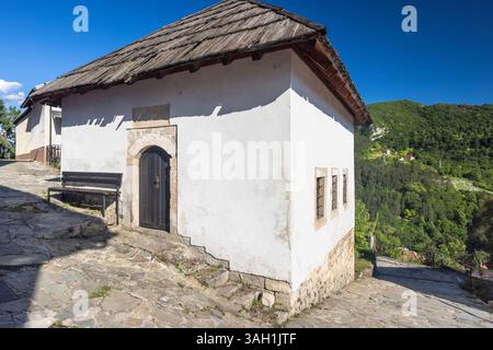 Jajce town in Bosnia and Herzegovina, Europe. Quaint white building with a dark wooden door and traditional roof, nestled in a hillside village under Stock Photo