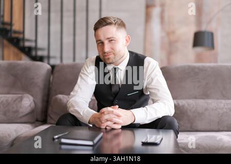 A man in business clothes sits at table with his arms folded in modern interior with soft lighting. focused look and professional style emphasize the Stock Photo
