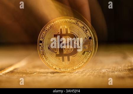 A fading, translucent, shiny gold Bitcoin rests on a textured wooden surface symbolizes the volatility of cryptocurrency, risk and uncertainty in the Stock Photo