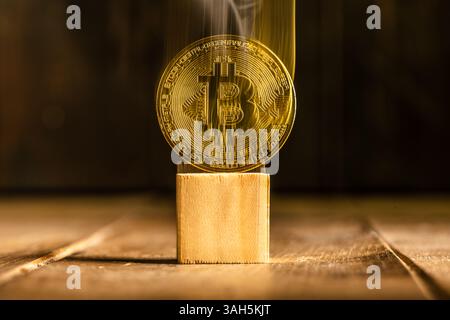 Smoke rising from a vanishing, translucent gold Bitcoin on a wooden block symbolizes the volatility of cryptocurrency, risk and uncertainty in the dig Stock Photo