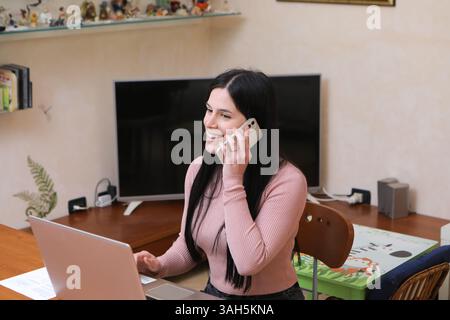 Happy businesswoman talking on mobile phone and using laptop while working from home Stock Photo