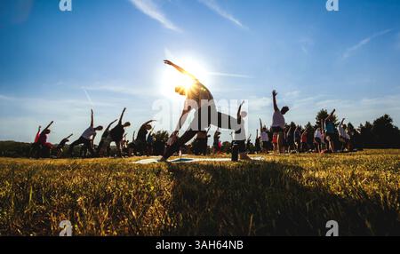 Group yoga class exercising outdoors in a field during sunset, performing stretching and balance poses. Stock Photo