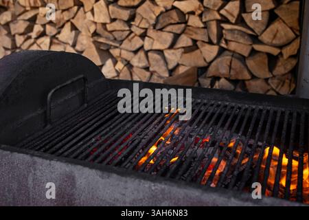 Empty burning flames grill with wood stacked in the background, soft focus Stock Photo