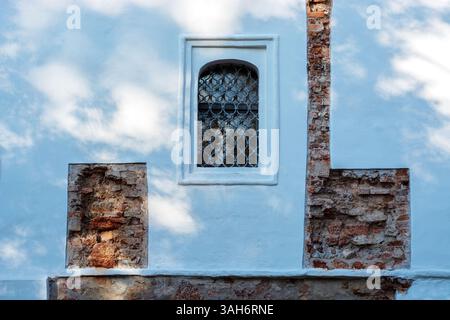 Arched window and fragments of old brick wall, on the background of white plastered wall on which the blue sky with clouds is reflected. From the seri Stock Photo
